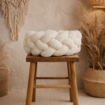 White braided pillow on a wooden stool with decorative elements in the background