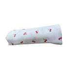 Baby Natur MAXI tetra muslin swaddle blanket with a white background and red cherry print. Made of 100% breathable cotton.