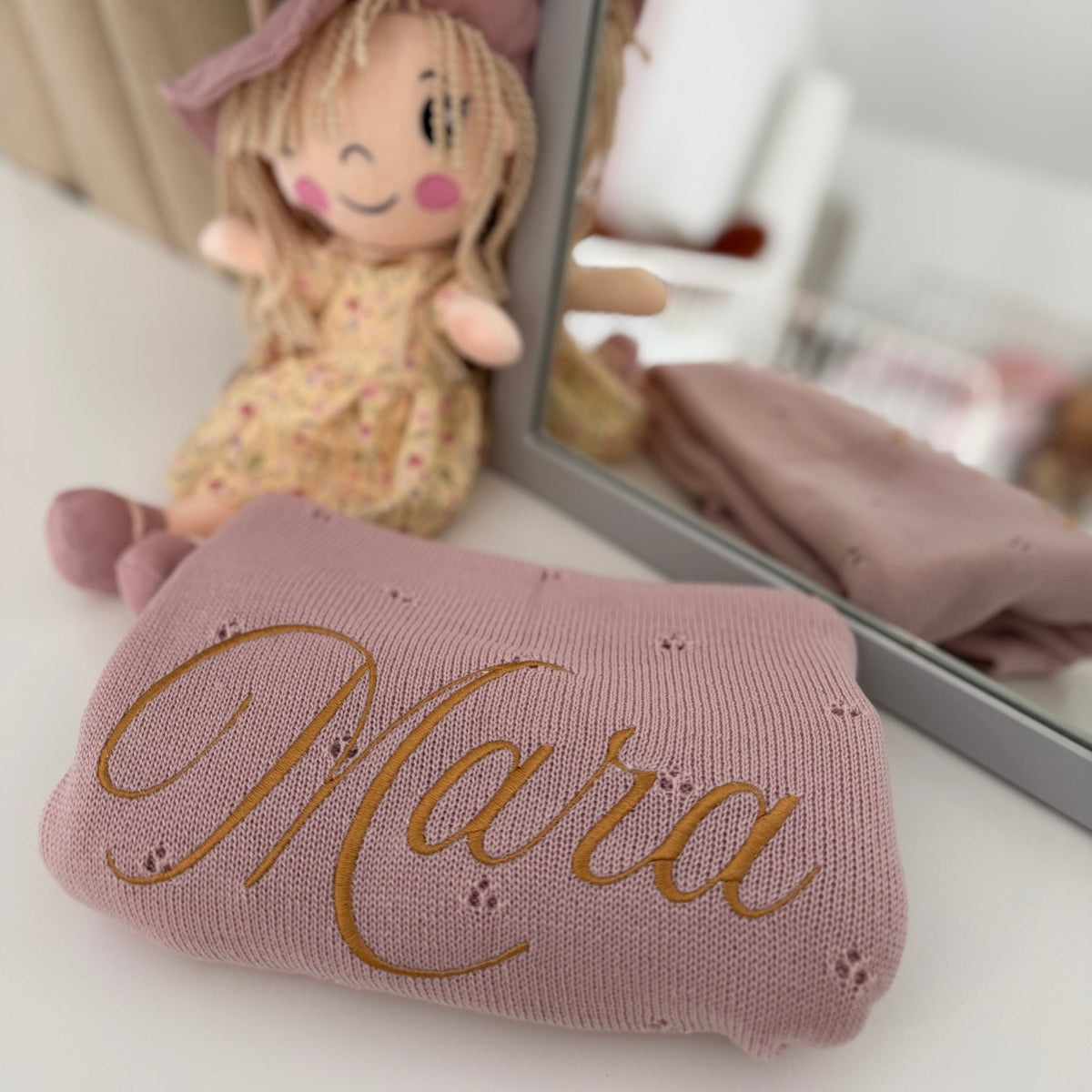 Pink plush toy with 'Mara' embroidered on it, next to a mirror.