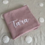Pink blanket with 'Tara' embroidery on a gray background with white dots