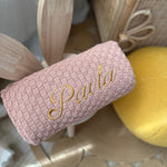 Pink textured roll with 'Paola' embroidery, wooden spoons, and a yellow ball on a neutral background