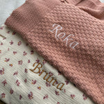Pink knitted blanket with embroidered names on a floral fabric background