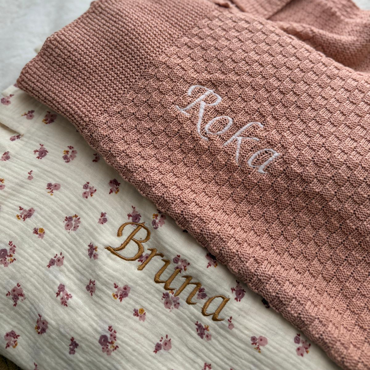 Pink knitted blanket with embroidered names on a floral fabric background