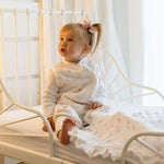 Baby Natur white muslin sleeping bag with floral print, featuring a baby with a pink bow in her hair sitting on a bed.