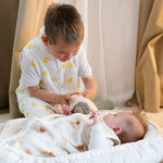 Baby Natur white 100% tetra muslin sleep sack with lemon print, worn by a boy. Baby in bassinet with fox print swaddle.