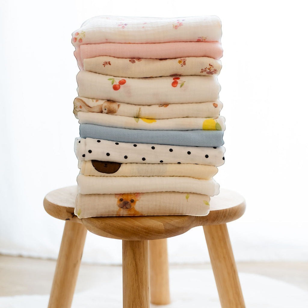 Baby NaturHere stack of 100% cotton muslin swaddle blankets with various prints including cherries, teddy bears, and dogs.