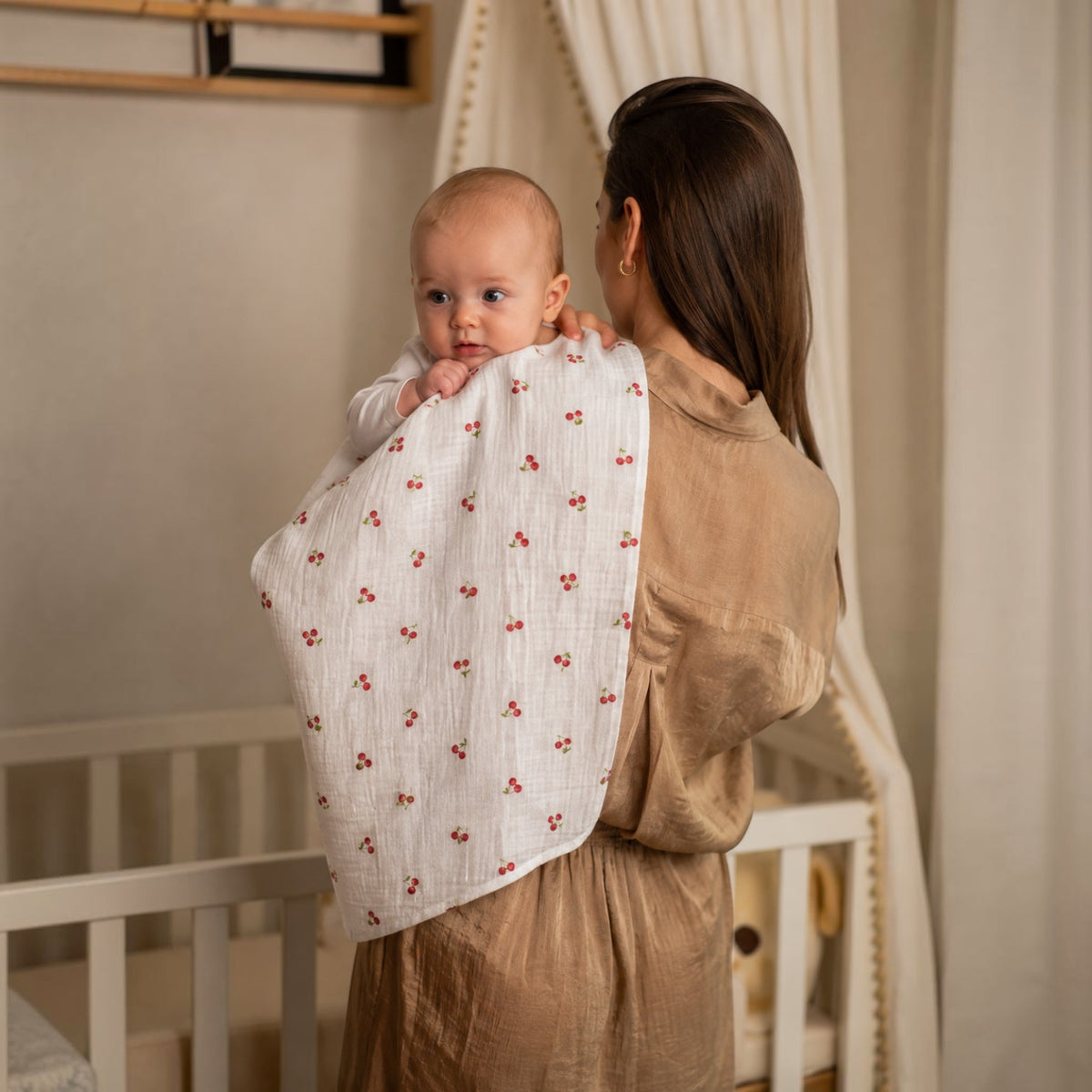Baby NaturHere white cotton muslin burp cloth with a red cherry print, draped over a mother's shoulder holding a baby.