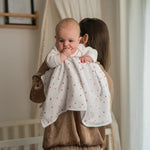 Baby NaturHere white cotton muslin swaddle blanket with small red hearts pattern, held by a person.